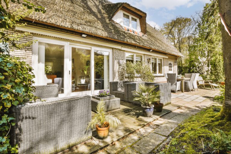 the outside of a house with some plants on the front and windows in the back, looking out to the garden