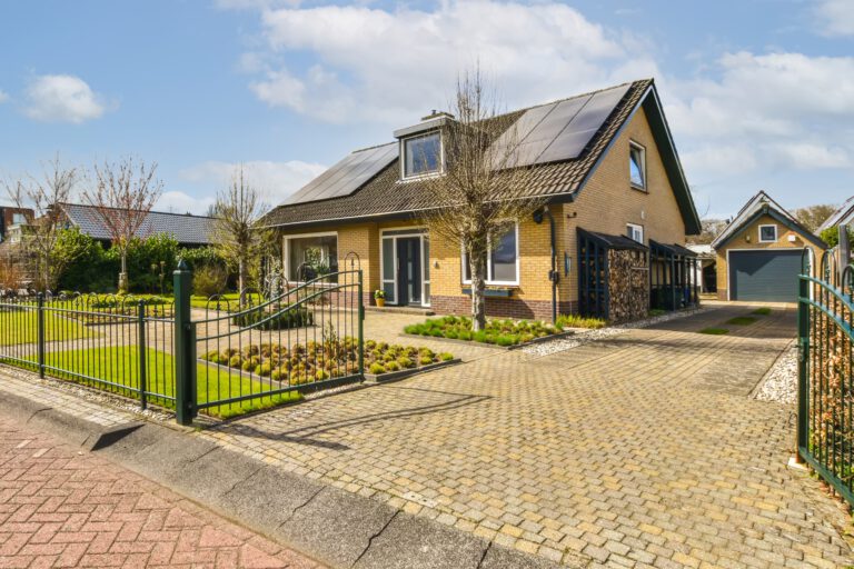 a house with solar panels on the roof and an iron fenced driveway leading up to the home's front door