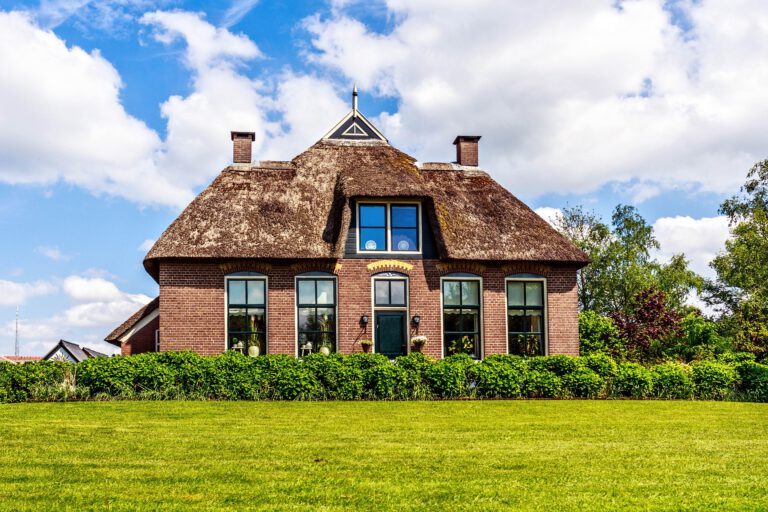 Traditional house with rustic thatched roof in a sunny day. Trees, flowers and bright blue sky with clouds on background. Giethoorn, Netherlands